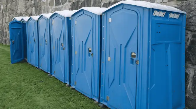 Row of blue portable toilets lined up on grass against a stone wall for event sanitation in Green Bay, WI