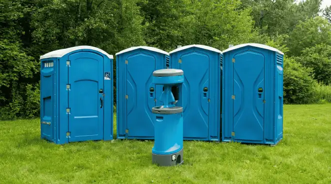 Four blue portable toilets and a matching hand washing station on grass near trees, a common sight at local outdoor events in Green Bay, WI