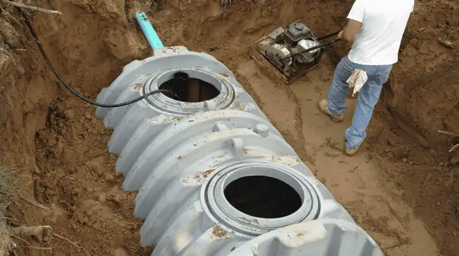 Septic tank installation showing a technician compacting soil around a new poly septic tank in an excavation pit in Green Bay, WI
